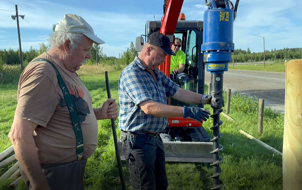 Paavo Laitinen ja Janne Laitinen auttavat konekuski Pekka Sutista tähtäämään aitatolpan reiän kohdalleen.