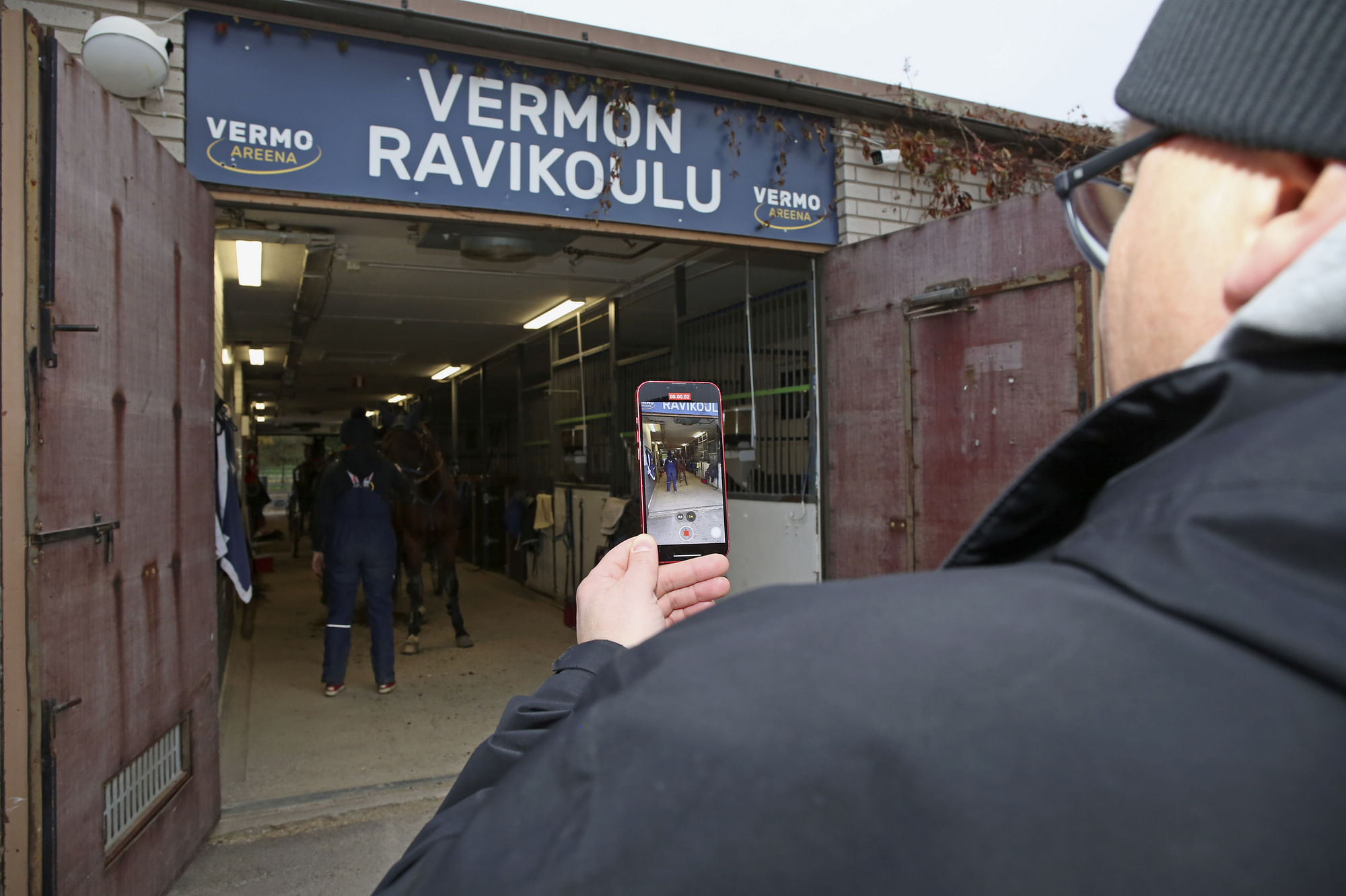 Raine Lehtonen ottaa videota Vermon tallialueella sijaitsevan ravikoulun edessä.