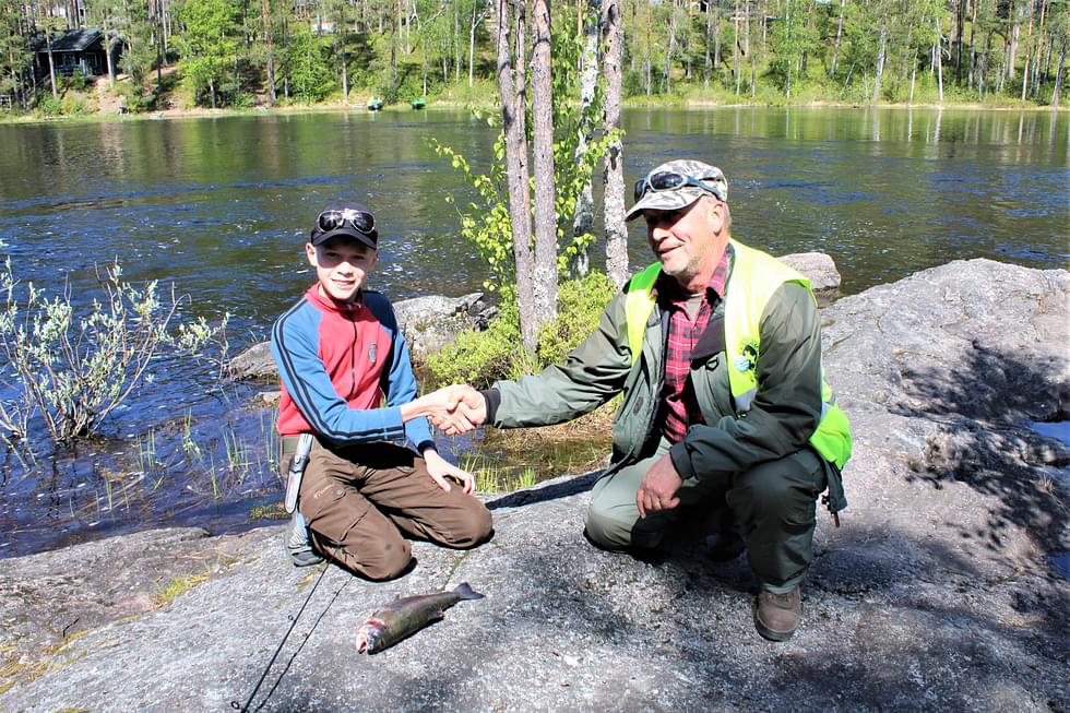 13-vuotias Taisto Rautarinta tuli jo kolmannen kerran toiselta puolelta Suomea Lieksaan kalastamaan. Matti Koivunen onnittelee Taistoa ensimmäisestä kirjolohesta.