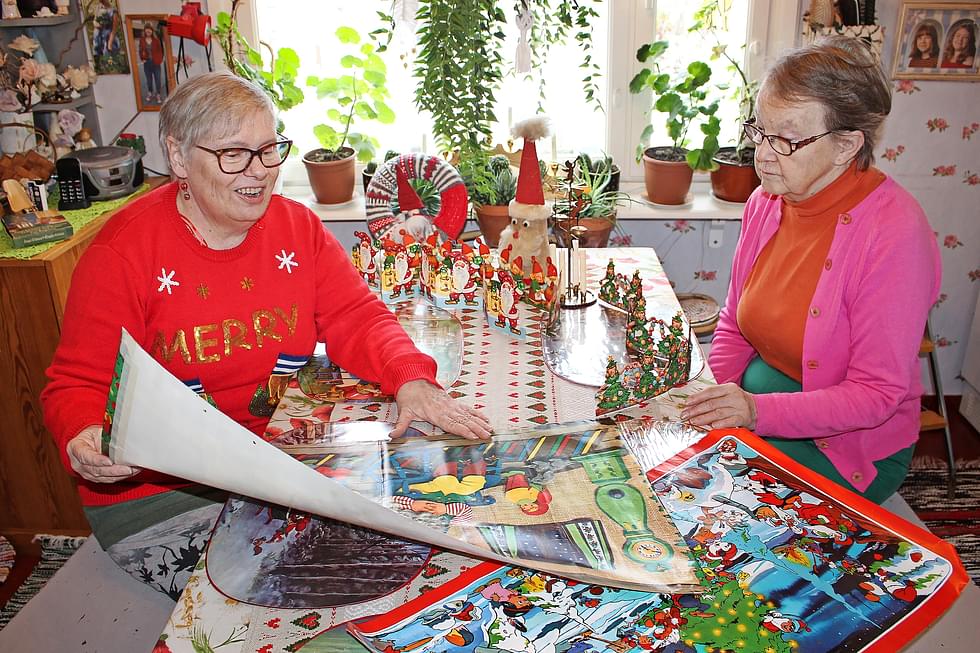 Leila Virnes ja Seija Antikainen tutkivat vanhoja joulutauluja. Pöydällä olevista koristeista vanhimmat ovat 1950-luvulta. 