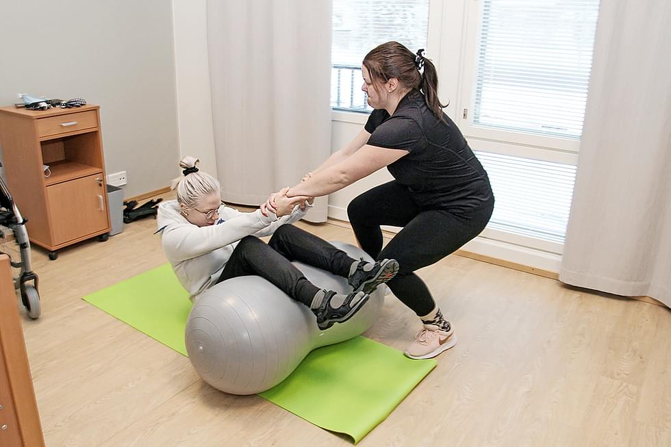 Attendo Havulinnassa työskentelevät lähihoitaja Senni Toivanen (vas.) ja fysioterapeutti Riina Pajarinen kertovat, että ihmisen saa autettua vähemmällä voimalla esimerkiksi ylös lattialta, kun tämä ponnistaa jaloillaan jumppapalloa vasten.