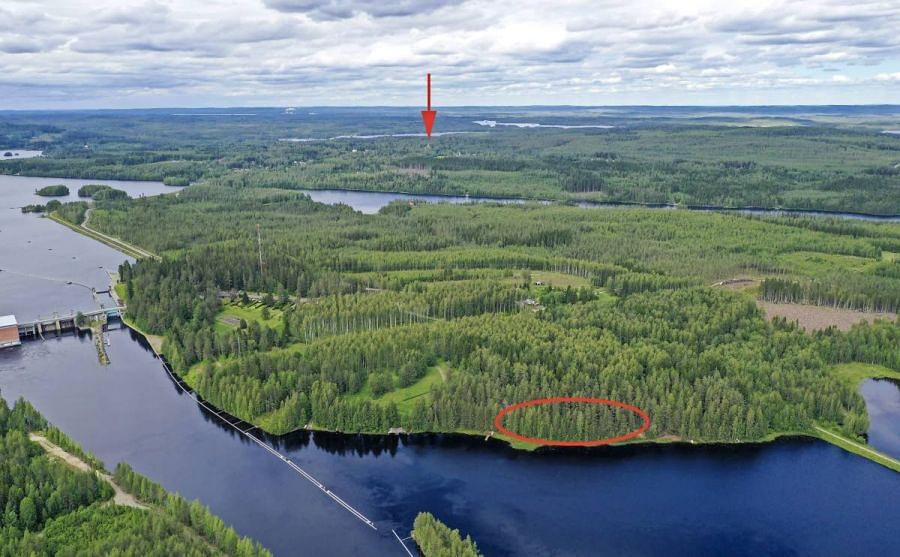 Enon Nesterinsaari (keskellä) ilmasta nähtynä kesäkuussa 2019. Kalmistoniemen muinaisjäännösalue on merkitty kuvan etualaan punaisella soikiolla ja mantereella sijaitseva Enon kirkko on osoitettu nuolella. Kuvattu pohjoiseen.