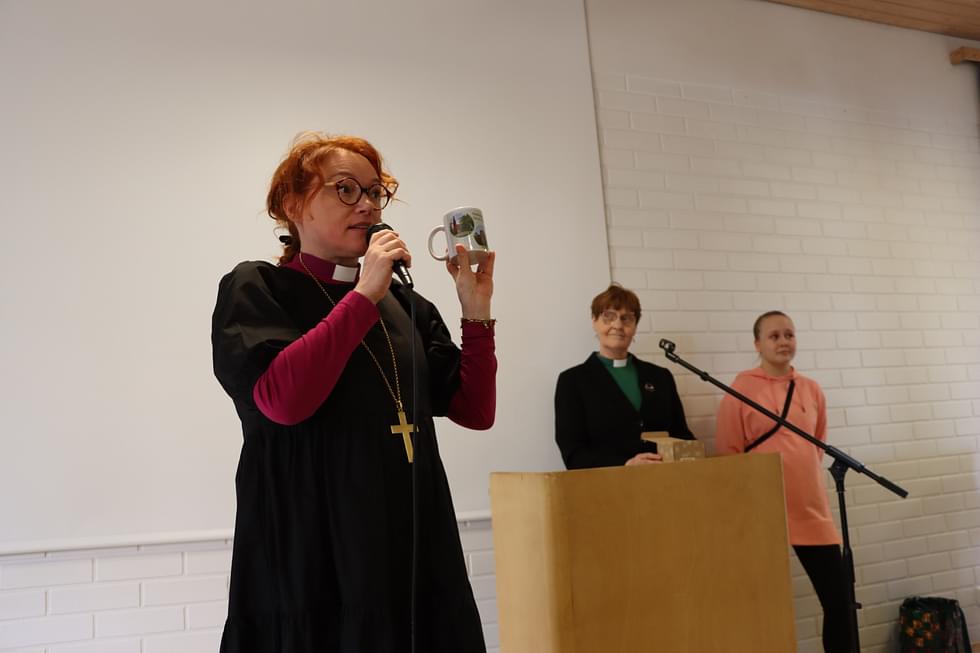 Piispa Mari Parkkinen sai lahjaksi Parikkalan seurakunnan mukin. Taustalla diakoni Jaana Vaittinen ja piispalle seurakuntalaisten tekemät kysymykset esittänyt Sara Jantunen.