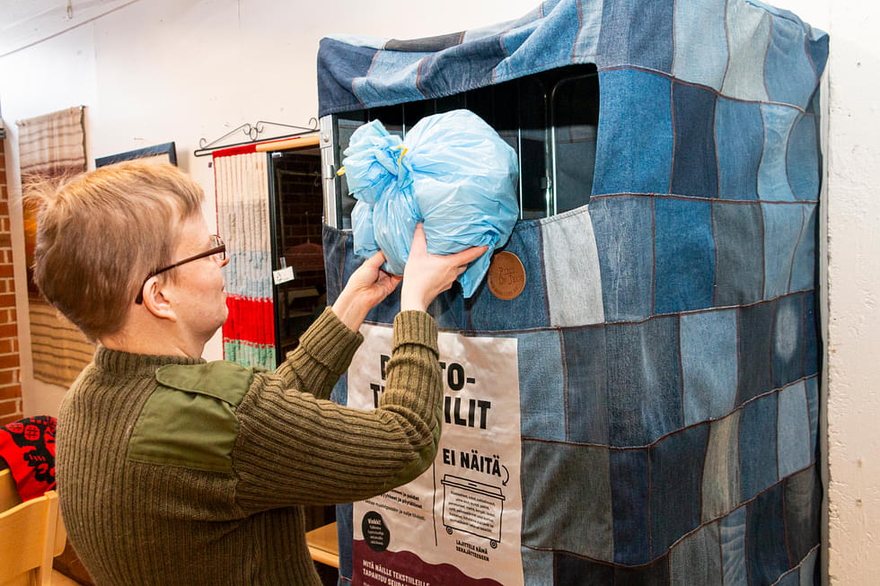 Helena Ikonen pudottaa pussillisen tekstiilejä rullakkoon, joka on päällystetty käytetyistä farkuista ommellulla kankaalla.